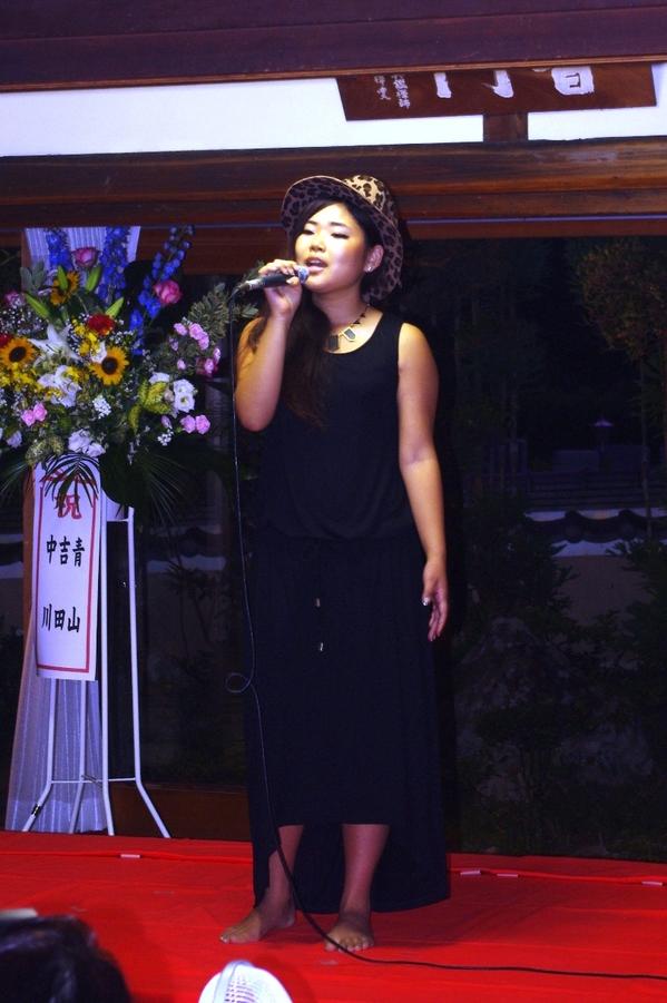 ヒョウ柄の帽子を被った遠山 恵さんがマイクを持ち、歌を歌っている写真